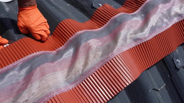 Installation of a roof ridge ventilation and sealing system. A roofer installs a ridge cap on a metal roof. Roofing work. Sandwich panels in the form of tiles.