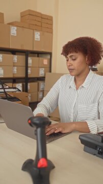 Woman stretches arms over laptop and cardboard boxes at a busy delivery office building while sitting at desk; calm relief.