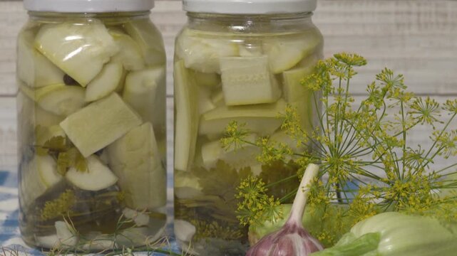 Homemade canned zucchini with dill and garlic, Authentic homemade pickled zucchini in glass jars with fresh garlic and dill on a rustic table.