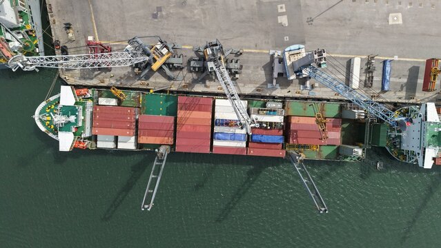 Riviera Beach, United States - 15 April 2026: Aerial view of a large container ship docked at the port with industrial cranes loading colorful cargo containers onto the vessel.