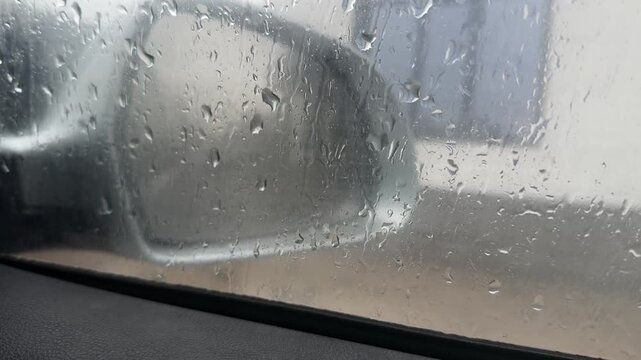 Car side mirror seen through wet window with rain drops