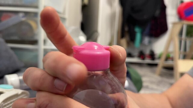 Hand holding small plastic bottle with pink cap containing liquid product