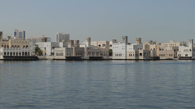 Dubai, United Arab Emirates - June 15, 2025: Traditional wind towers and buildings lining the shore of Dubai Creek.