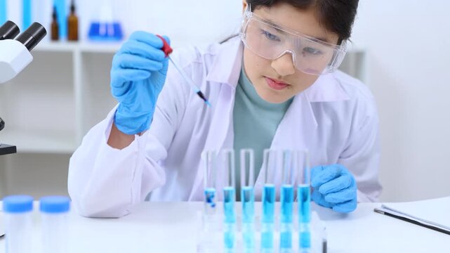 Teen scientist girl conducting science test by carefully evaluating blue solution in laboratory. Science, laboratory, experiment, and research demonstrate academic progress and practical skills.