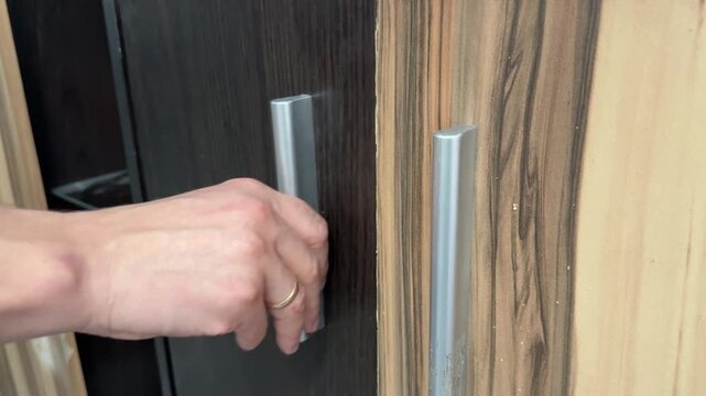 A person opening and closing a wooden cabinet door