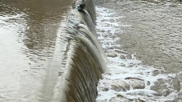 Water flowing over small dam outdoors creating foam and strong current
