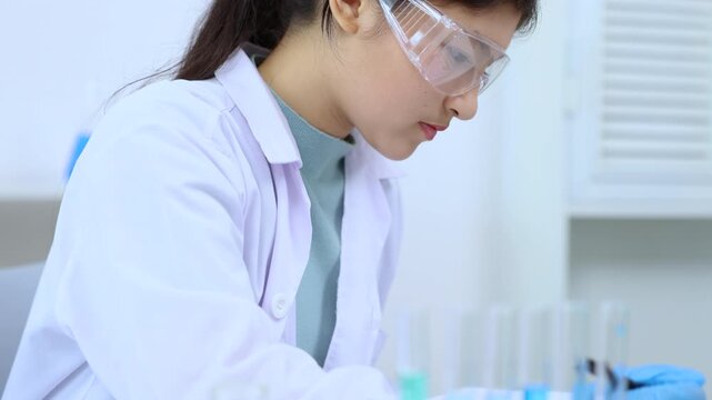Asian female science student in lab coat writes notes in a laboratory notebook while analyzing experiment, engaging in science, laboratory, scientist, experiment, and research documentation.