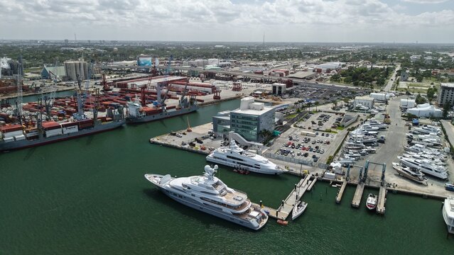 Port of Palm Beach, United States - 15 April 2026: Aerial view of Riviera Beach showing luxury yachts docked at the marina alongside industrial cargo ships and container terminals under a cloudy sky.