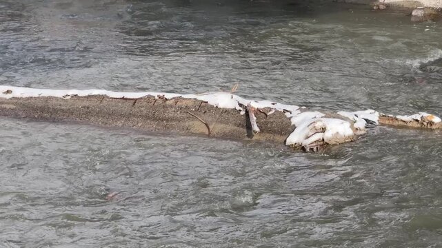 Flowing river water near a narrow concrete barrier with small patches of snow outdoors, winter nature scene, quiet landscape, cold season
