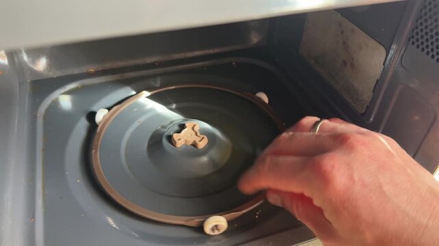 Hand installing the glass turntable plate inside a microwave oven. Close up of placing rotating tray on the central support of kitchen microwave appliance for proper food heating