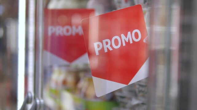 Red promotional sticker with the word promo on a supermarket refrigerator door. Shallow depth of field shot highlighting a special offer for customers inside a grocery store during a sale