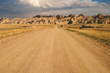 Badlands landscape with hills and dramatic clouds above a dirt road heading into the distance © Daniel Thornberg