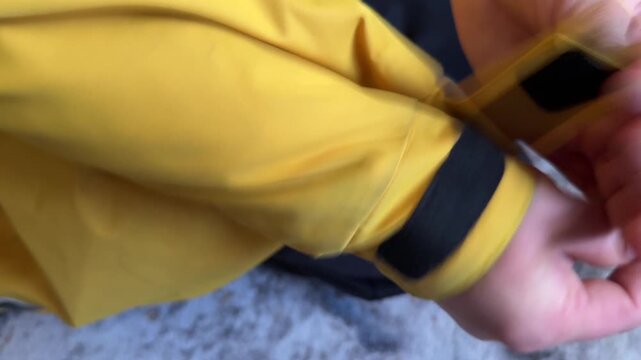 A person fastens and unfastens the Velcro strap on a yellow jacket sleeve to adjust the fit
