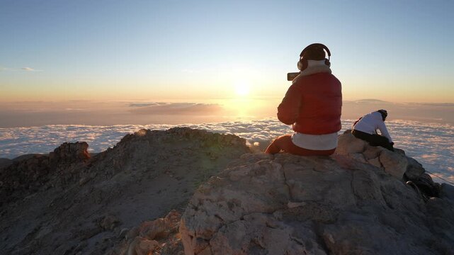 Person capturing stunning sunrise above clouds on mountain top