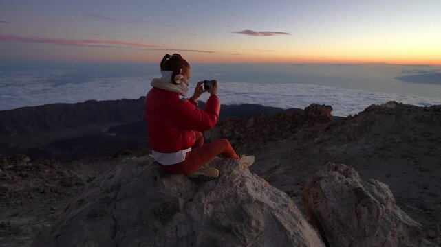 Woman traveler photographing sunrise from mountain top