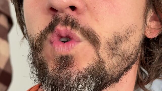 Close-up of man making a kissing gesture with pursed lips. Beard and mustache visible