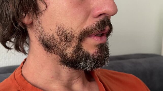 Man blows air through tightly pressed lips. Beard and mustache visible. Playful or tension-releasing gesture in indoor setting