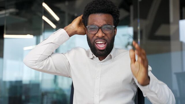 Angry african american businessman arguing talking on a video call looking in camera sitting in office. Excited dissatisfied manager dealing with stressful business situation. Boss scolds subordinate