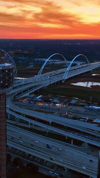 Flying along the spherical top of Reunion Tower in Dallas, Texas, USA at sunset. Complicated road system, Dallas Margaret Mcdermott Bridge and city view at the backdrop of orange sky. Vertical video