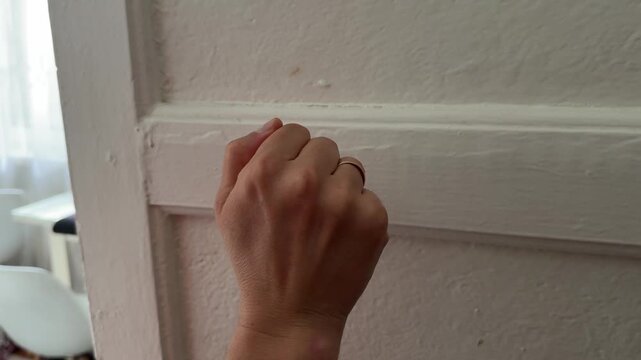 Hand knocking on closed interior door. Waiting to enter room, polite gesture, everyday home interaction in close up view
