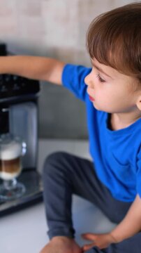 Cute child sits near the coffee machine. Little kid preparing cappuccino at home. Vertical video