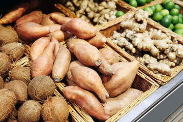 Obraz premium Sweet potatoes in baskets. Fresh market produce background. Ginger coconuts limes detail. Organic grocery display. Healthy tropical ingredients. Natural food selection.