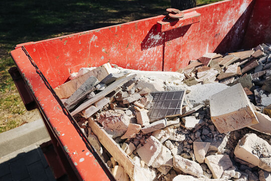 Red construction dumpster with rubble. Renovation waste container background. Broken tiles debris detail. Demolition cleanup scene. Industrial disposal material. Building site trash view.