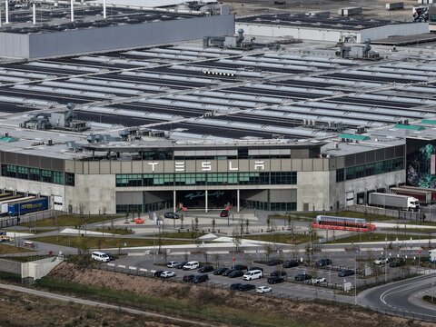 Grunheide, Germany - 18 April 2026: Aerial view of the Tesla Gigafactory Berlin-Brandenburg featuring the main entrance, solar panels on the roof, and parked vehicles.