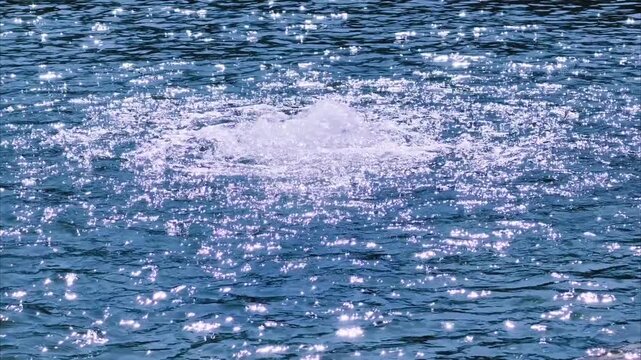 Slow motion bright sapphire blue water surface with bubbles, expanding ripple waves and shimmering reflections. Calming abstract background footage for wallpaper and screensaver in 4K Dolby Vision HDR