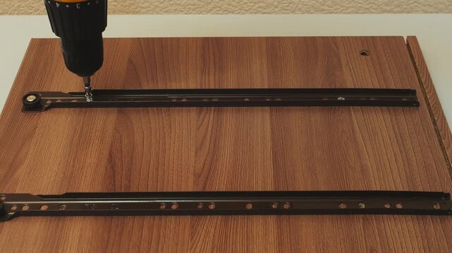 A man assembles furniture and screws drawer slats. Medium shot.