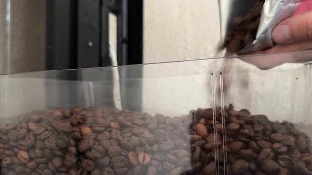 Hand pouring roasted coffee beans into machine hopper for drink preparation
