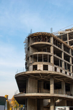 A construction tower crane operates against the backdrop of an unfinished building and a blue sky. Concept: Urban construction pollutes the air