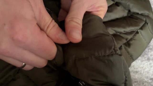 A person fastens and unfastens metallic snap buttons on a green padded jacket