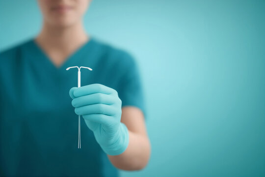Doctor wearing scrubs and gloves presenting an intrauterine device (IUD) on a clean blue background. Birth control method, contraception, gynecology, family planning, reproductive health concept
