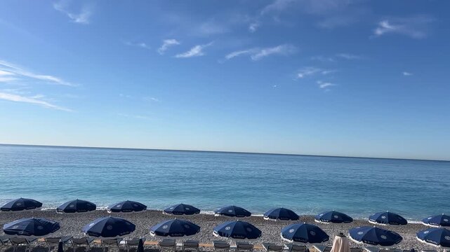 Serene Seascape: A picturesque view unfolds, where azure waters meet the infinite horizon under a tranquil sky, embraced by a row of umbrellas. France, Nice,