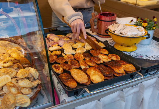 endor uses wooden tongs to grill small golden oscypek cheese pastries and bacon-wrapped snacks on a hot plate at a market food stall. Good for street food, local cuisine, grilled cheese, snack prepara