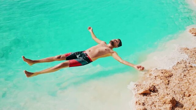 young man floating in bright blue salt pool wearing bathing suit in Siwa Oasis, Egypt