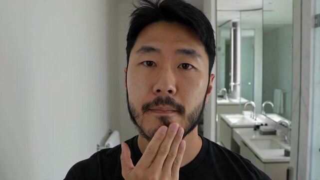 A Young Asian Man Applies Moisturizer Cream to His Face, Focusing on Skincare and Beard Hydration