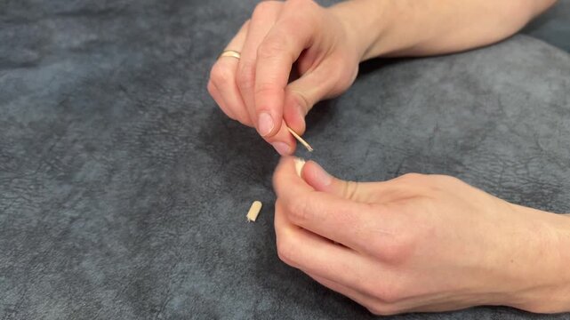 A person breaks a thin wooden stir stick into several smaller pieces using both hands