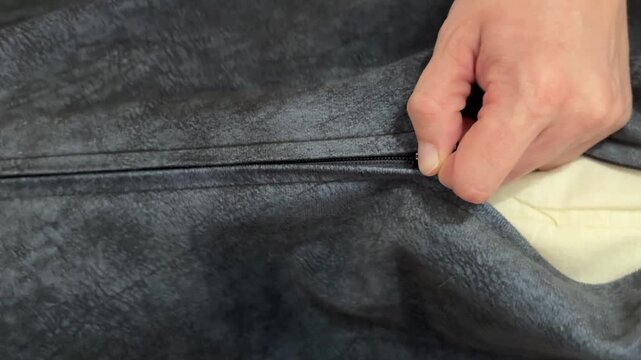 A person zipping up a grey cushion cover