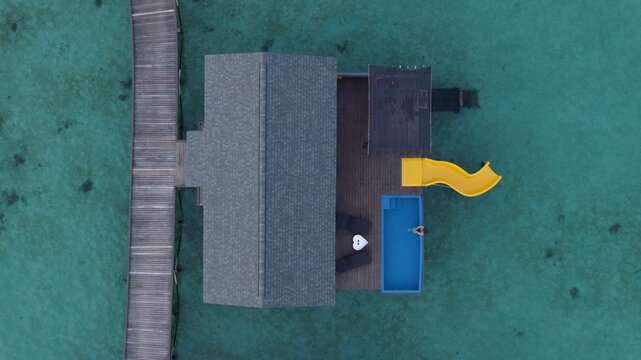 Semporna, Malaysia - 17 April 2026: Aerial view of SKY Resort Timbun Mata Island and Reef with its wooden walkway, private pool, and yellow slide over turquoise water.