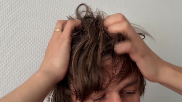 A man scratches or massages his scalp with both hands. Fingers move through messy brown hair