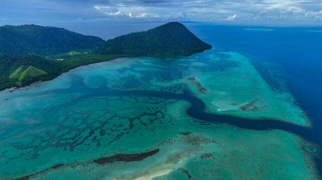 Semporna, Malaysia - 13 August 2025: Aerial view of the turquoise coral reefs and lush green hills of Timbun Mata Island under a dramatic cloudy sky.