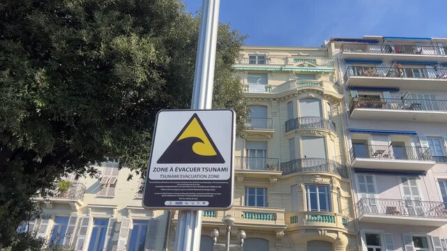 Tsunami Zone Sign: The warning sign of a tsunami zone stands tall, cautioning against potential dangers in coastal areas with the backdrop of a charming, light-colored building. 