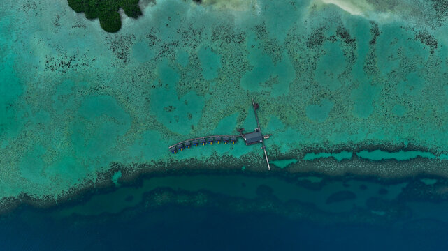 Semporna, Malaysia - 13 August 2025: Aerial view of SKY Resort Timbun Mata Island and Reef featuring overwater bungalows and wooden walkways over vibrant coral reefs and turquoise sea.
