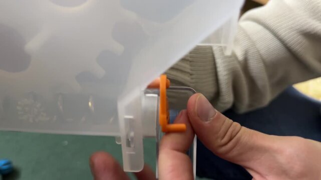 Hands adjusting plastic container with orange latch mechanism during equipment assembly