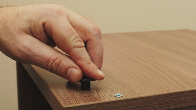 A person's hand is screwing in a piece of furniture with drawers. Medium shot.