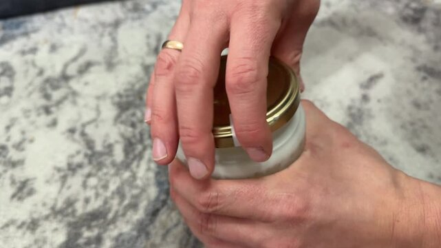 A person opens a sealed glass jar containing beef tallow by twisting the metal lid
