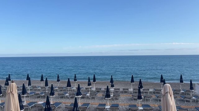 Serene Beach Day: A mesmerizing display of folded parasols line the shore, gazing out at the endless stretch of the sea under a clear sky. A perfect getaway scene. 