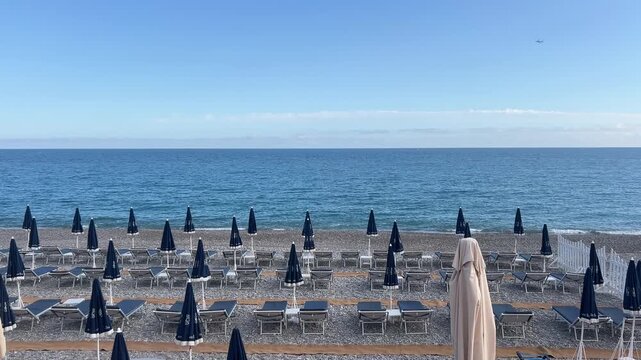 Beach Umbrellas at Seaside: A serene coastal scene unfolds with rows of neatly arranged beach umbrellas and lounge chairs facing the boundless expanse of the ocean under a clear blue sky.